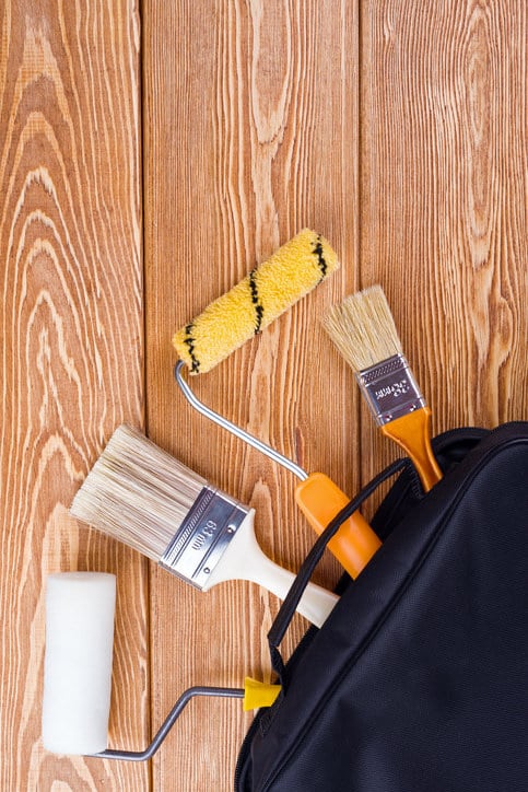 Mur blanc en train d’être peint avec un rouleau de peintre Outils professionnels de peinture en bâtiment à moitié sortis de leur étui de rangement posé sur des planches en bois