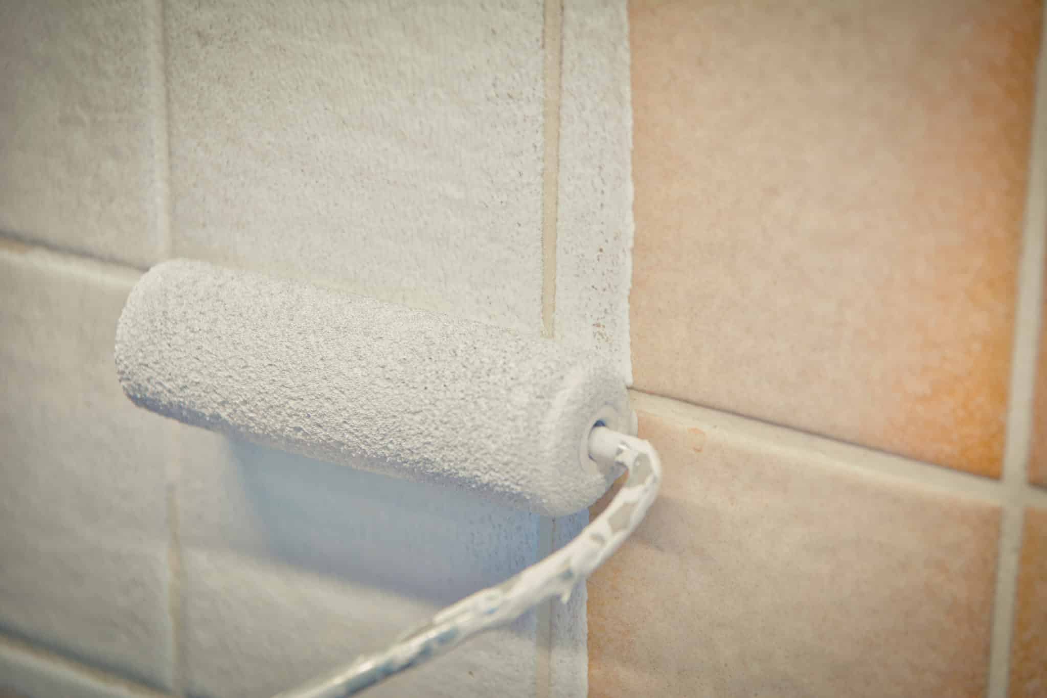 peinture-sur-carrelage Vieux carrelage mural beige en train d'être repeint en blanc avec un mini rouleau